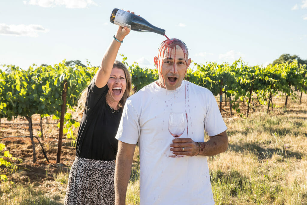 Whitney Scotto pouring a bottle of wine onto Paul Scotto in the vineyard